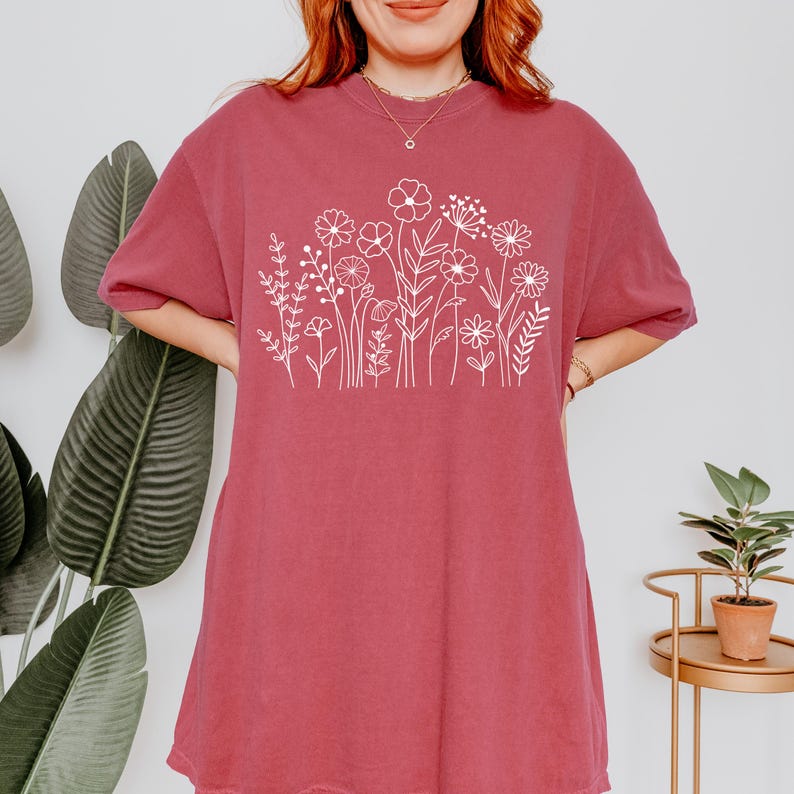 May include: A maroon oversized t-shirt with a white outline of a floral design. The design features various flowers and leaves.