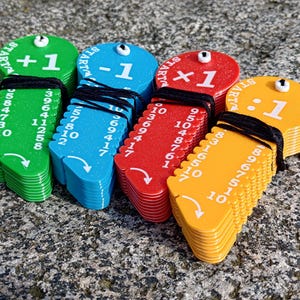 Può includere: Quattro pile di chiavi di plastica colorate con numeri e simboli matematici. Le chiavi sono verdi, blu, rosse e gialle. I simboli sulle chiavi sono +1, -1, ×1 e ÷1.