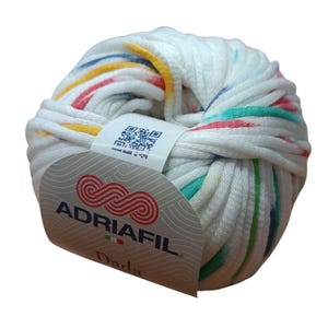 Può includere: Un gomitolo di filato bianco con strisce colorate di rosso, giallo, verde e blu. Il filato è etichettato "ADRIAFIL Dada".