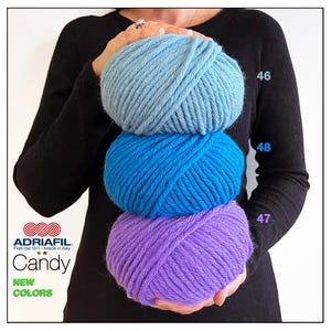 Può includere: Tre gomitoli di lana impilati uno sopra l'altro. Il gomitolo superiore è azzurro, il gomitolo intermedio è blu e il gomitolo inferiore è viola. La lana è etichettata "Adriafil Candy" e ha i numeri 46, 48 e 47 sul lato.