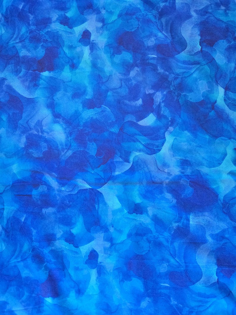 May include: A close-up of a fabric with a vibrant blue watercolor design. The pattern features swirling shapes in shades of deep indigo, cerulean, and light blue, creating a dynamic and artistic effect. The fabric appears soft and flowing.