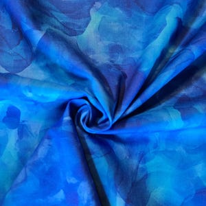 May include: A close-up of a fabric with a watercolor-like design. The fabric features shades of blue, from light turquoise to deep indigo, creating a flowing, abstract pattern. The fabric is gathered, showing folds and shadows.