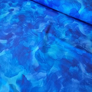 May include: A bolt of fabric with a watercolor-style floral pattern in shades of blue. The design features overlapping, abstract shapes in varying tones, creating a flowing, artistic effect. The fabric appears to be lightweight and suitable for apparel or home decor.