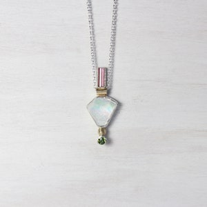 Könnte beinhalten: Eine Halskette aus Silber mit einem Anhänger, der einen weißen, schillernden Stein, einen rosafarbenen Turmalin und einen grünen Edelstein enthält.
