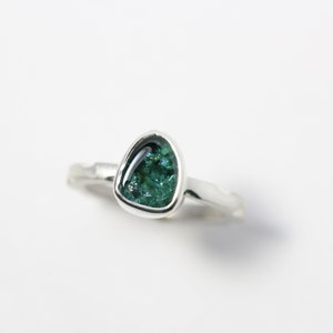 May include: A silver ring featuring a green gemstone set in a bezel setting. The gemstone is teardrop-shaped and has a sparkly, iridescent finish.