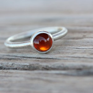 May include: A silver ring with a round, orange gemstone set in a bezel setting.