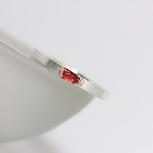 May include: A silver band ring with a red gemstone set in a rose gold bezel.