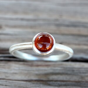 K&ouml;nnte beinhalten: Ein silberner Ring mit einem roten Edelstein, der in einer Zargenfassung gefasst ist.