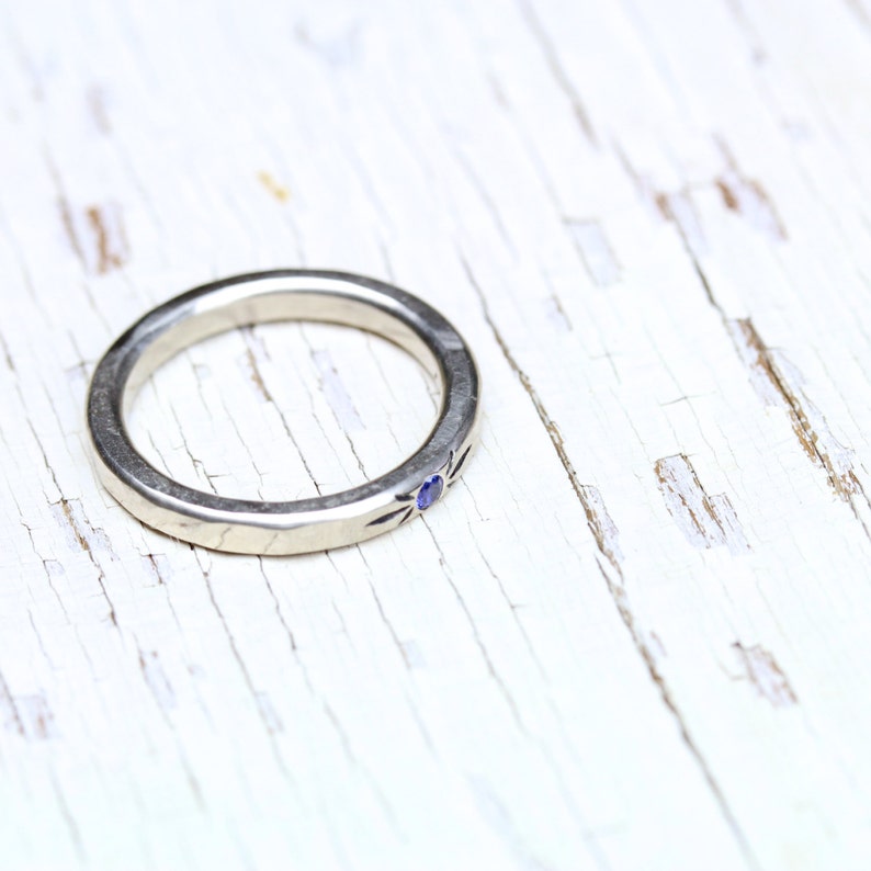 May include: A silver ring with a small blue gemstone set in the center. The ring is on a white wooden surface.