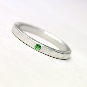 May include: A silver band ring with a small green gemstone set in the center.