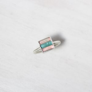 Könnte beinhalten: Ein silberner Ring mit einem quadratischen Edelstein, der in der Mitte eingesetzt ist. Der Edelstein ist ein mehrfarbiger Turmalin in Rosa- und Grüntönen.