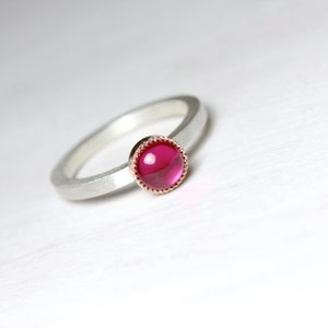 May include: A silver ring with a pink gemstone set in a rose gold bezel. The ring has a simple, elegant design.