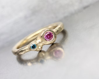 May include: A gold ring with two gemstones. The larger gemstone is pink and the smaller gemstone is blue.