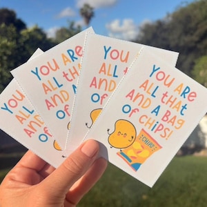 May include: A hand holds several white cards with the text "You are all that and a bag of chips!" in colorful lettering. Each card features a cartoon potato and a bag of chips.