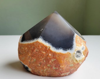 Op de afbeelding: Een groot, natuurlijk gevormd, bruin, wit en zwart agaat kristal met een puntige top. Het kristal heeft een ruw, getextureerd oppervlak.