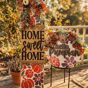 Peut inclure: Un panneau en bois rectangulaire haut avec le texte HOME sweet HOME et un panneau rond avec le texte hello Pumpkin. Les deux panneaux pr&eacute;sentent des citrouilles peintes orange et violettes, des feuilles vertes, des n&oelig;uds en tissu &eacute;cossais.