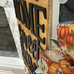 Peut inclure: Un panneau vertical en bois pr&eacute;sentant le texte d&eacute;coup&eacute; noir Home Sweet Home superpos&eacute; sur un fond en bois clair. Le panneau est d&eacute;cor&eacute; d'un ruban en toile de jute &agrave; motifs de citrouilles orange et de feuilles vertes fix&eacute; sur le c&ocirc;t&eacute;.