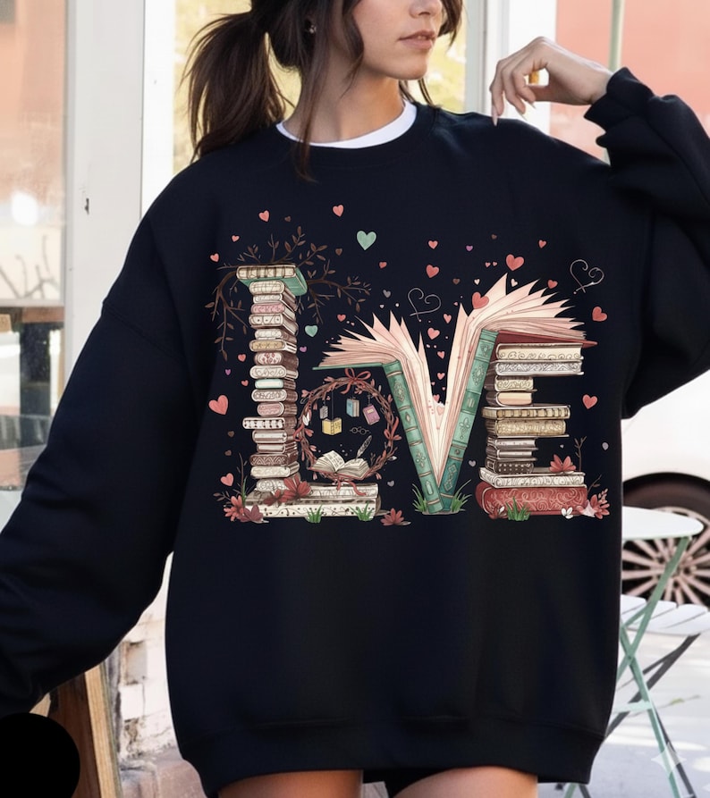 May include: Black sweatshirt with the word "LOVE" spelled out with stacks of books. The "L" and "E" are made of books, and the "O" is a wreath with books and a quill. Pink and green hearts are scattered around the design.