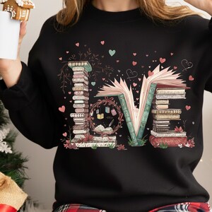 May include: Black sweatshirt with the word "LOVE" spelled out with stacks of books and an open book. The "O" is a wreath with books and hearts. Pink and teal hearts are scattered around the design.