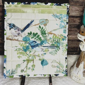 May include: A quilted fabric case with a zipper closure, featuring a print of blue birds perched on branches with green leaves and blue flowers. The case has a green stripe at the top and a blue border.