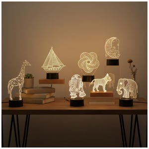 May include: A selection of decorative LED lamps with wireframe designs, including a giraffe, a sailboat, and a dog. Each lamp sits on a black base. The lamps are displayed on a wooden table, with each lamp's height varying.