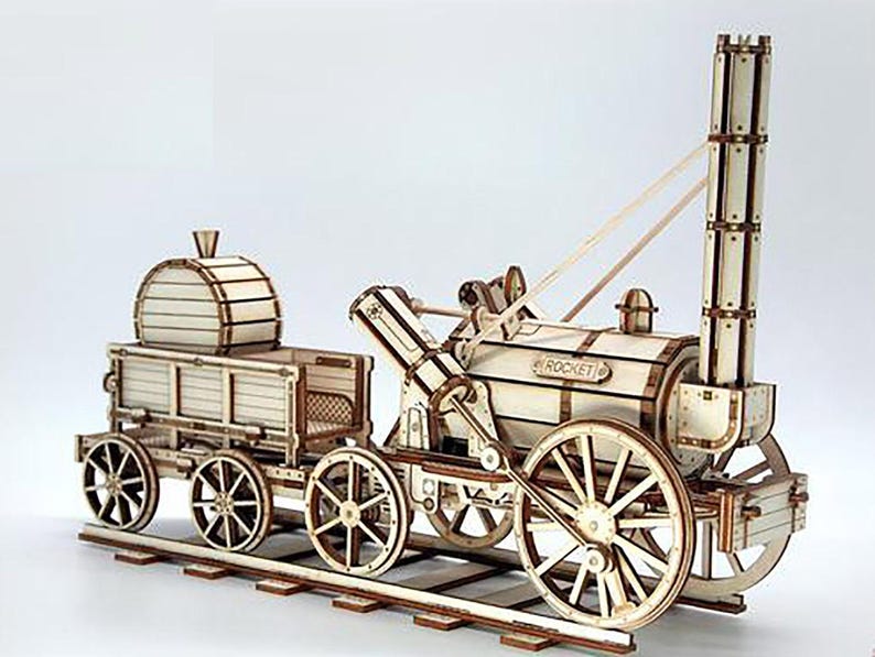 May include: A wooden model of a vintage steam train, featuring a locomotive and a separate car. The model is constructed from light-colored wood with visible details like wheels, a smokestack, and the word "ROCKET" on the side.