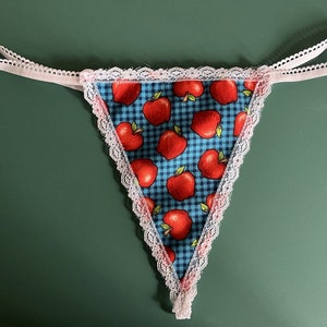 May include: A white lace trimmed triangle shaped garment with a blue and white gingham pattern and red apple print.