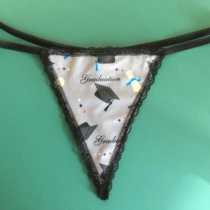 May include: Black lace lingerie with a gray and white graduation cap print. The print includes the word "Graduation" and a blue and yellow diploma.