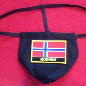 Puede incluir: Bolsa de tela negra con un parche de la bandera noruega roja, blanca y azul y la palabra "NORWAY" en letras amarillas. La bolsa está unida a una correa negra ajustable.