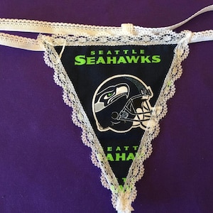 May include: White lace trimmed black underwear with a Seattle Seahawks logo and a green and blue helmet graphic.