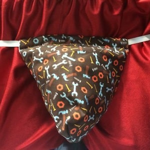 May include: A brown fabric pouch with a white elastic band. The pouch is decorated with a repeating pattern of small tools, including wrenches, screws, and nuts. The tools are in shades of blue, yellow, and orange.