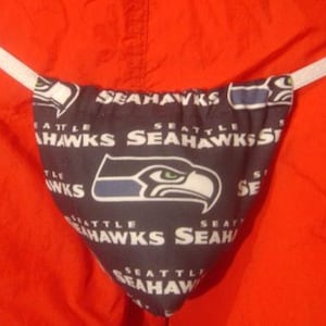 May include: A blue and black fabric thong with the Seattle Seahawks logo repeated on the fabric. The thong has white elastic straps.