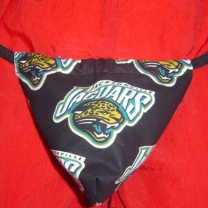 May include: Black and teal fabric thong with the Jacksonville Jaguars logo repeated on the fabric. The logo features a jaguar head with the words "Jacksonville Jaguars" written in white.