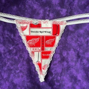 May include: White lace trim g-string with a red and white pattern featuring the Detroit Red Wings logo and the words "Detroit Red Wings".