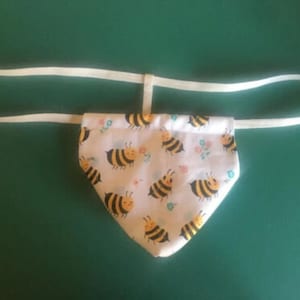 May include: White fabric with a bee pattern and a white elastic band. The fabric is a triangle shape.