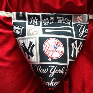 May include: A white and blue fabric pouch with a New York Yankees theme. The pouch has a drawstring closure and is decorated with baseballs, bats, and the team's logo.