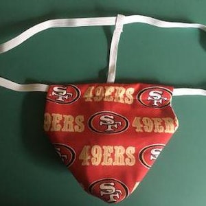 May include: A red and gold athletic supporter featuring the San Francisco 49ers logo and team name. The supporter has a white elastic waistband and a triangular pouch design.