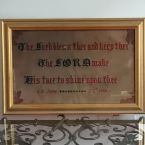 以下が含まれることがあります： 金色のフレームに入った額装されたアートワーク。「The Lord bless thee and keep thee, The LORD make His face to shine upon thee」と書かれています。テキストの下には「J.E. June 22 1880」と書かれています。