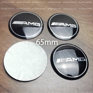 Puede incluir: Cuatro emblemas circulares de 65 mm con acabado negro brillante, logotipo AMG plateado y borde plateado. Tres emblemas muestran el diseño frontal, mientras que uno está volteado para mostrar su reverso adhesivo blanco liso.