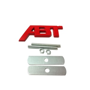 May include: Red metal car emblem with the letters "ABT" in a bold, sans-serif font. The emblem comes with two metal mounting plates and two screws.