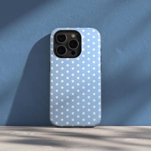 May include: A light blue phone case with a white polka dot pattern. The case is designed to fit a smartphone and has a camera cutout. The case is made of a smooth material and is shown against a blue background.