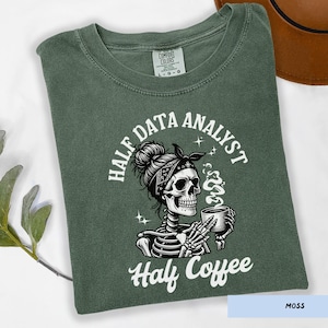 May include: Moss green t-shirt with a graphic of a skeleton wearing a bandana and holding a coffee cup. The text reads "HALF DATA ANALYST" and "Half Coffee" in white. The shirt is a Comfort Colors brand.