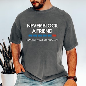 May include: Gray t-shirt with the text "NEVER BLOCK A FRIEND" in white. Below the text is a row of blue and red rectangles. The phrase "(UNLESS IT'S A SIX-POINTER)" is below the main text.