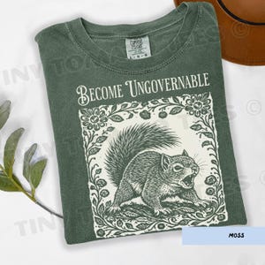 May include: Moss green t-shirt with the text "Become Ungovernable" above a detailed illustration of a squirrel. The squirrel is surrounded by a floral border. The shirt is a Comfort Colors brand, size L-G.