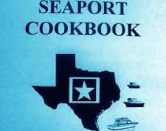 May include: The cover of a blue cookbook titled "The Great Texas Seaport Cookbook: Recipes of the Texas Gulf Coast Communities". The cover features a black silhouette of the state of Texas with a white star in the center. There are three small black silhouettes of ships in the bottom right corner.
