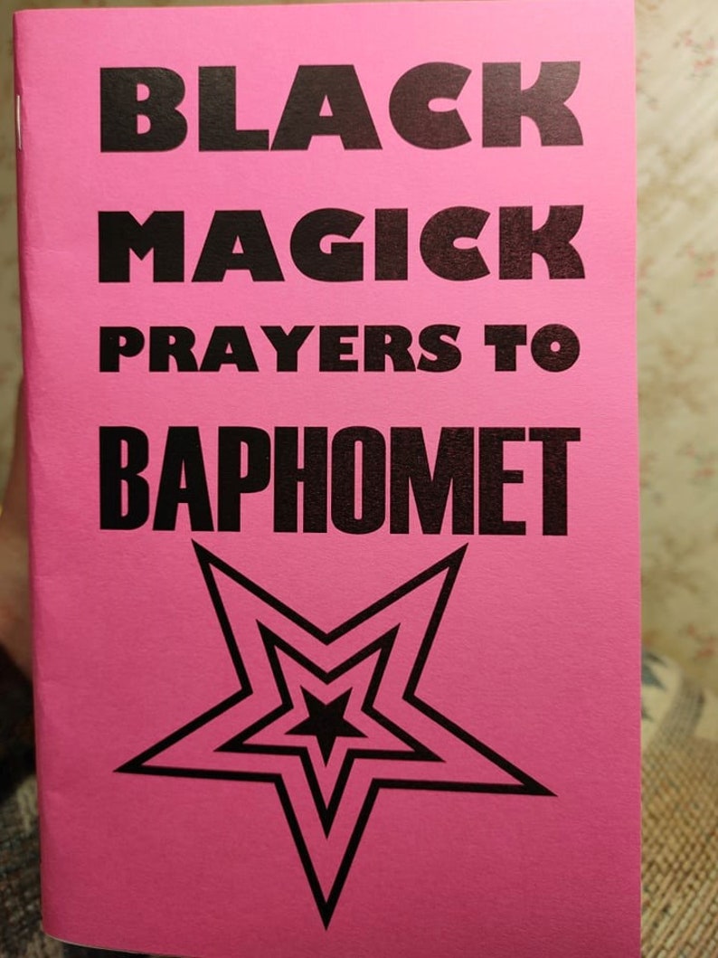 Op de afbeelding: Een roze boekje met de titel "Black Magick Prayers to Baphomet" in zwarte tekst. Een zwarte vijfpuntige ster met een kleinere ster erin is gecentreerd op de omslag.