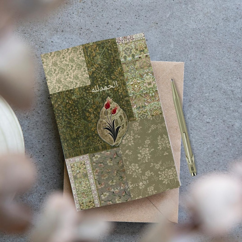 Pu&ograve; includere: Un diario decorativo con un design patchwork nei toni del verde e beige. La copertina presenta un motivo floreale e il testo arabo "الحمد لله". Una penna dorata &egrave; appoggiata accanto al diario su una busta neutra.
