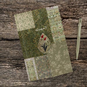 Pu&ograve; includere: Un diario decorativo con un design patchwork nei toni del verde e beige, con motivi floreali e decorativi. La copertina include testo arabo e un emblema floreale stilizzato con tulipani rossi. Una penna d'argento &egrave; appoggiata accanto al diario.