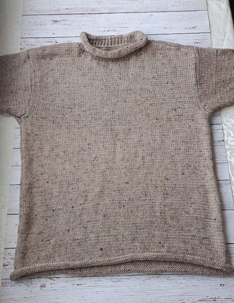 May include: A beige, short-sleeved sweater with a ribbed roll neck collar and hem. The knitwear has a speckled texture, with flecks of darker brown and red throughout the fabric. The sweater is laid flat, showcasing its simple, classic design.