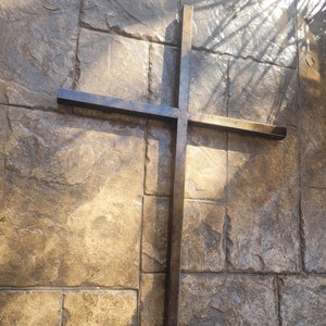 May include: A large black metal cross mounted on a stone wall. The cross is made of thick metal and has a rustic finish.